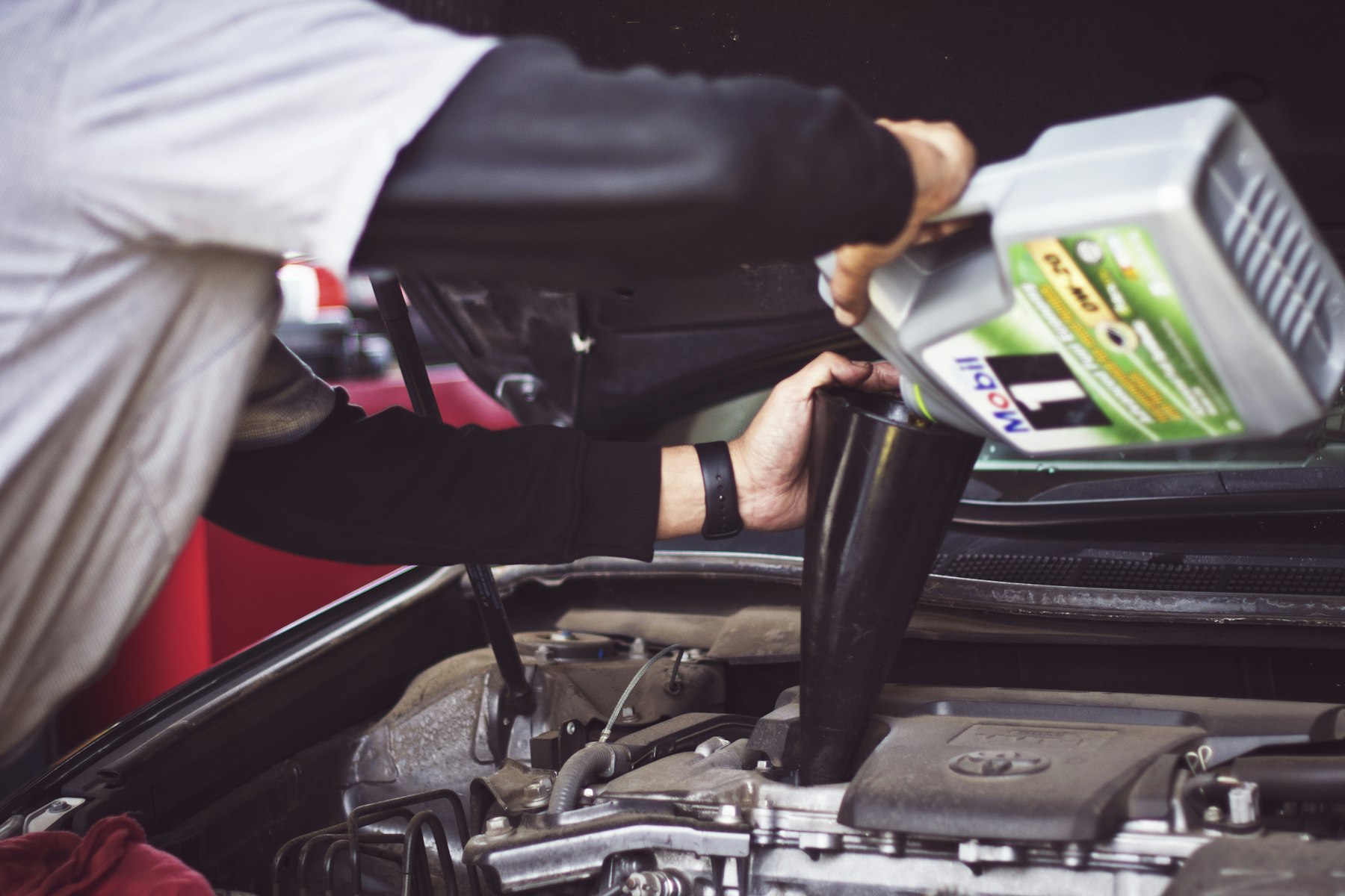 Technician pouring fresh oil into a car engine during a service
